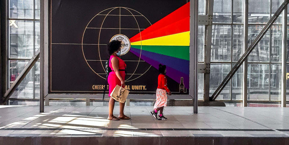 A woman and her child look perfectly in place as they walk past a billboard at a train station.