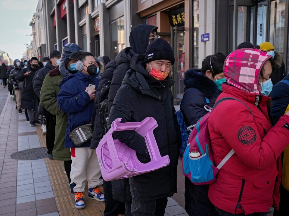 A man carries a plastic chair as he and hundreds of residents line up to visit a store selling 2022 Winter Olympics memorabilia in Beijing, Monday, Feb. 7, 2022. The race is on to snap up scarce 2022 Winter Olympics souvenirs. Dolls of mascot Bing Dwen Dwen, a panda in a winter coat, sold out after buyers waited in line overnight in freezing weather.