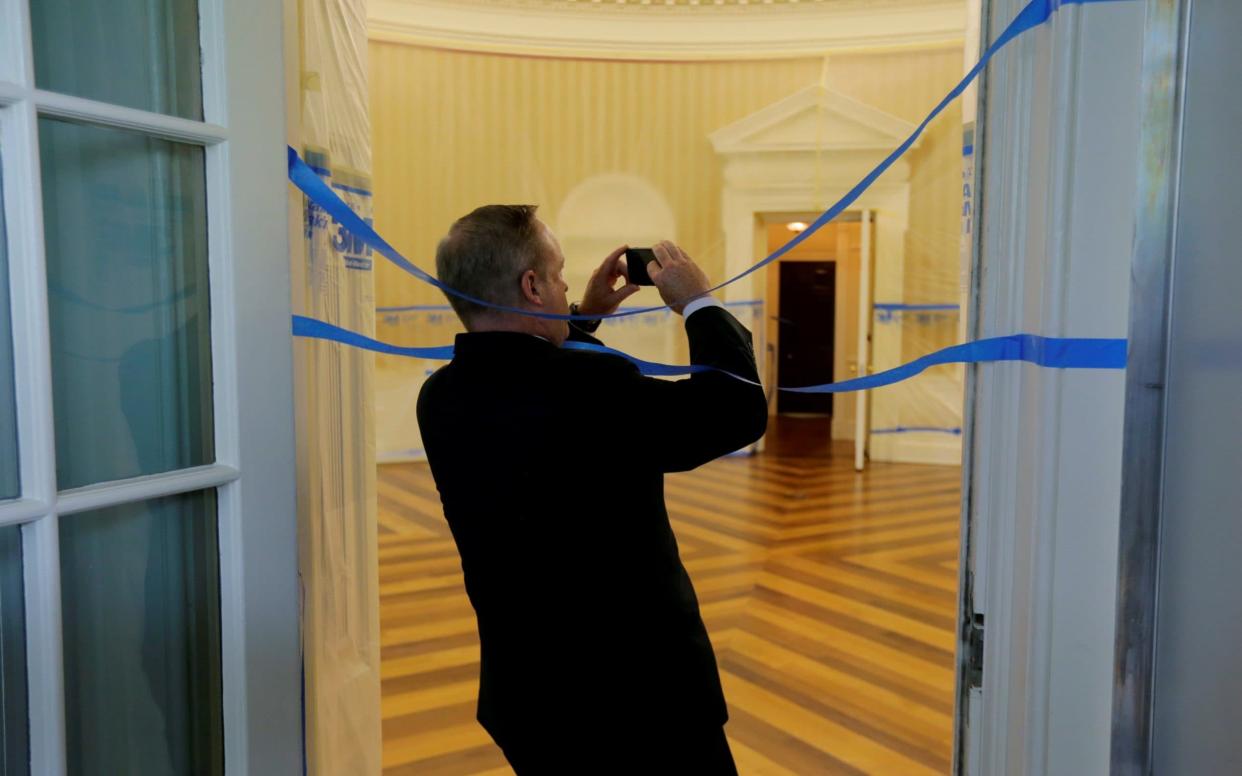 Former White House Press Secretary Spicer wraps himself in tape as he takes photos of the Oval Office emptied of all furniture, carpet and other decor during renovations at the White House in Washington - REUTERS