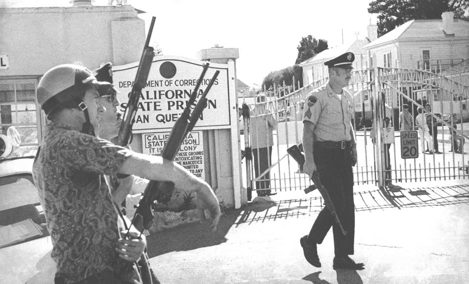FILE - Police officers from surrounding Marin County towns, supplementing prison guards, all heavily armed, stand guard outside the main gate of California's San Quentin prison, where an attempted escape took the lives of three officers and four convicts, Aug. 21, 1971. The infamous state prison on San Francisco Bay that has been home to the largest death row population in the United States will be transformed into a lockup where less-dangerous prisoners will receive education, training and rehabilitation under a new plan from California Gov. Gavin Newsom. (AP Photo/Ott, File)