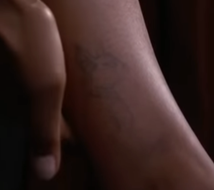 A close-up of Simone's ankle featuring a faint outline of a sphynx cat tattoo