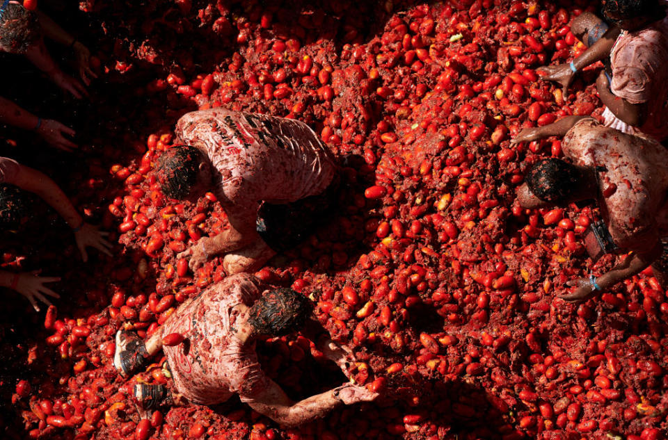 People are engaging in a tomato fight, covered in smashed tomatoes, as part of the La Tomatina festival in Spain