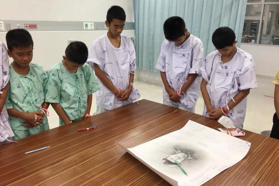 Some of the rescued football team bowing their heads respectfully in front of a sketch of the Thai Navy SEAL diver who died while trying to rescue them (AP)