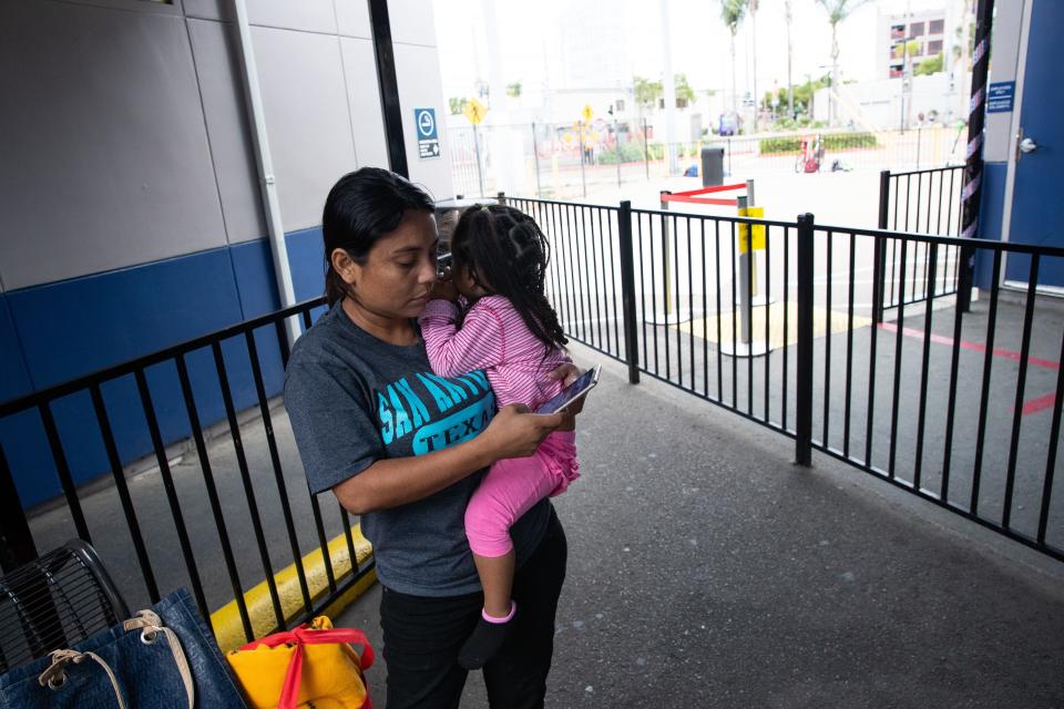 SAN DIEGO, Calif.  – Delmy López, 31, un migrante hondureña, le envía un mensaje de texto a su cuñado mientras carga en brazos a su hija de dos años, Perla, en la estación Greyhound al final de un viaje de dos días de San Antonio, Texas, a San Diego, el 29 de junio del 2019.