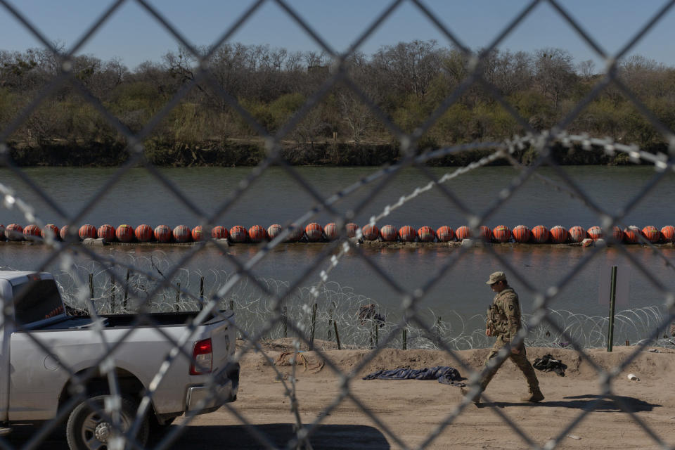 A soldier, seen through a chain link fence, walks past a line of buoys in Eagle Pass, Texas.