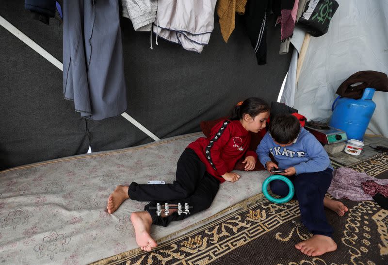 Laila Al-Sultant, a displaced Palestinian girl who was wounded in an Israeli strike that killed her father, plays with her brother Khaled inside their makeshift shelter, in Rafah in the southern Gaza Strip