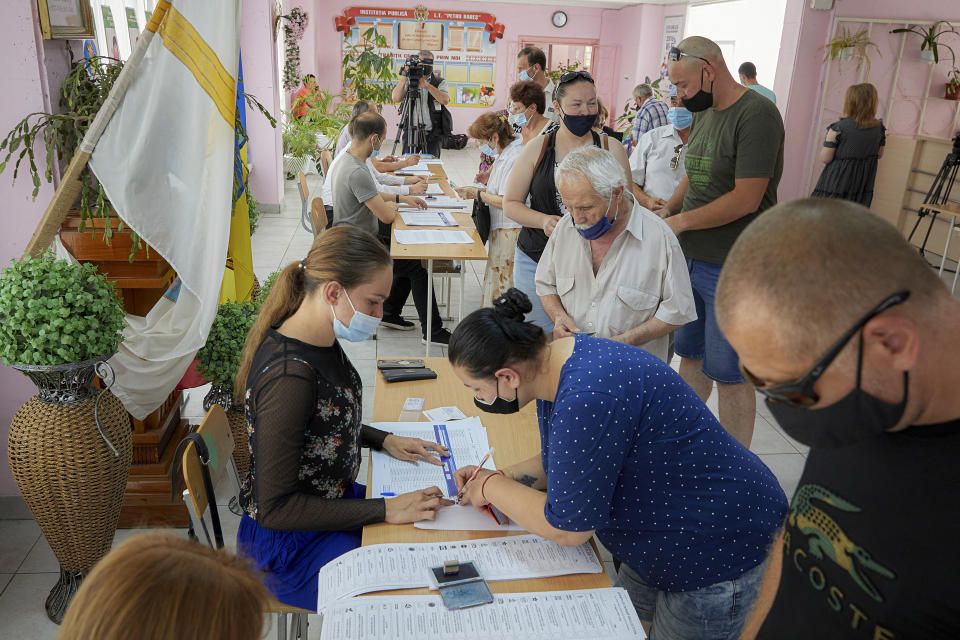 Moldovan citizens queue to receive ballots in a snap parliamentary election, in Chisinau, Moldova, Sunday, July 11, 2021. Moldovan citizens vote in a key snap parliamentary election that could decide whether the former Soviet republic fully embraces pro-Western reform or prolongs a political impasse with strong Russian influence. (AP Photo/Aurel Obreja)