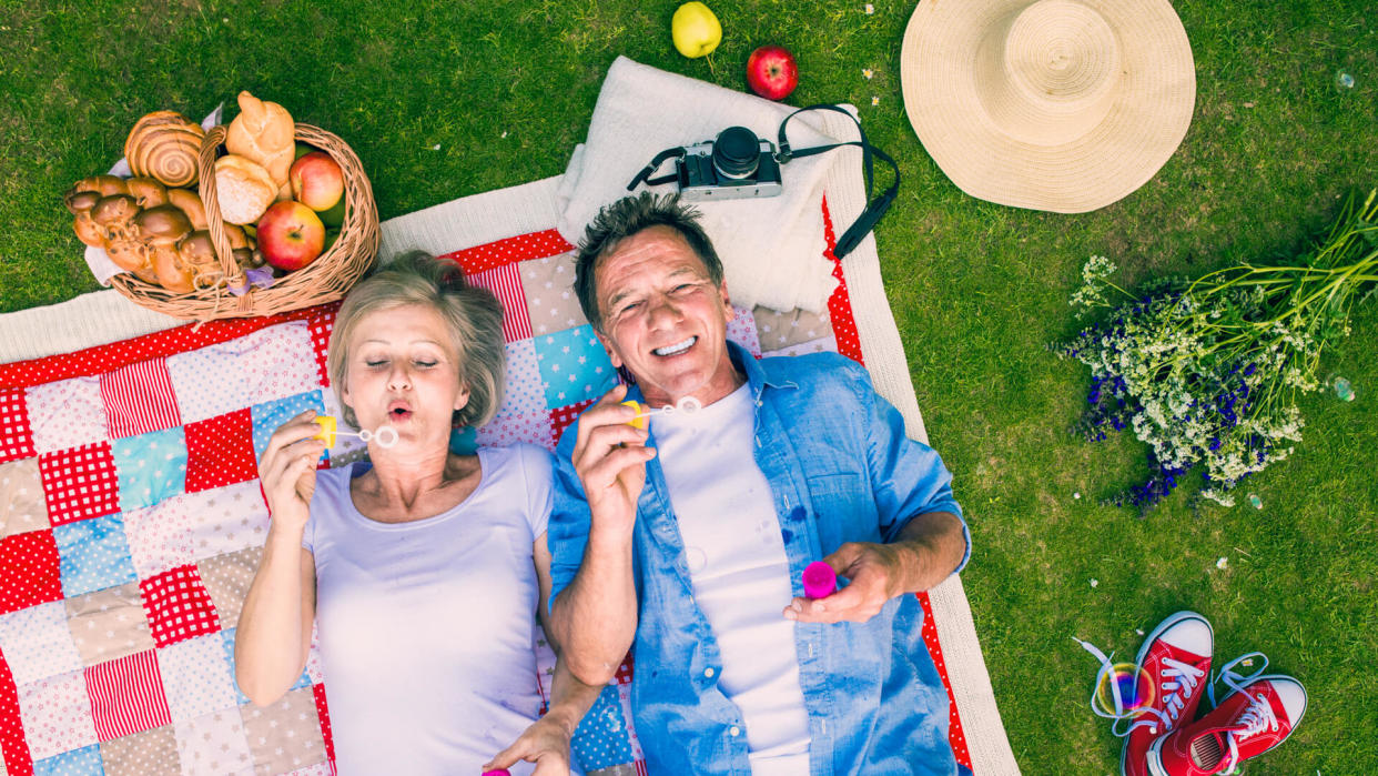 Beautiful seniors having a picnic in nature and blowing bubbles.