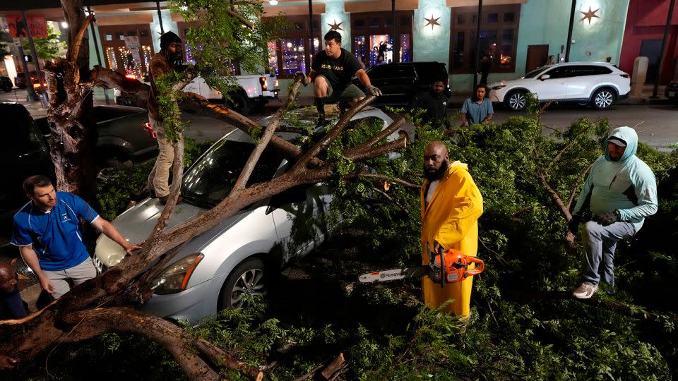 Rapper Trae tha Truth, in yellow, cuts fallen tree limbs on top of a car in the aftermath of a severe thunderstorm that passed through Houston on Thursday. - David J. Phillip/AP