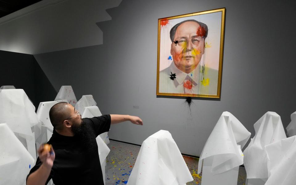 Chinese dissident artist Badiucao throws paintballs at an image of Mao Zedong