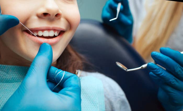 Girl smiling while a dentist and dental assistant use tools during a dental checkup