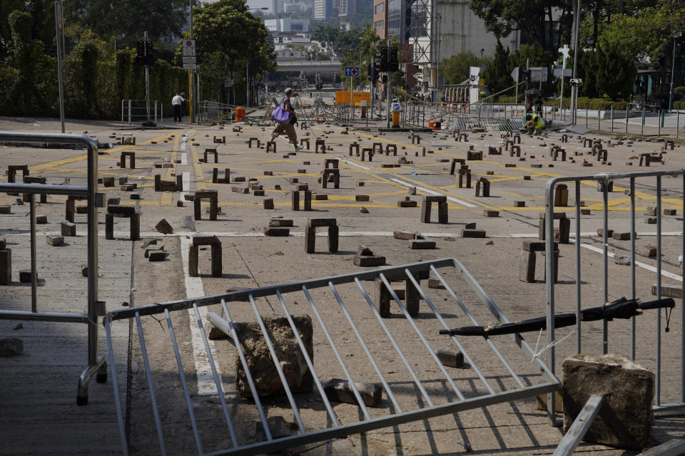 A woman walks by an intersection scattered with bricks and barricades set by pro-democracy protesters outside the Hong Kong Baptist University, in Hong Kong, Wednesday, Nov. 13, 2019. Police increased security around Hong Kong and its university campuses as they brace for more violence after sharp clashes overnight with anti-government protesters. (AP Photo/Vincent Yu)