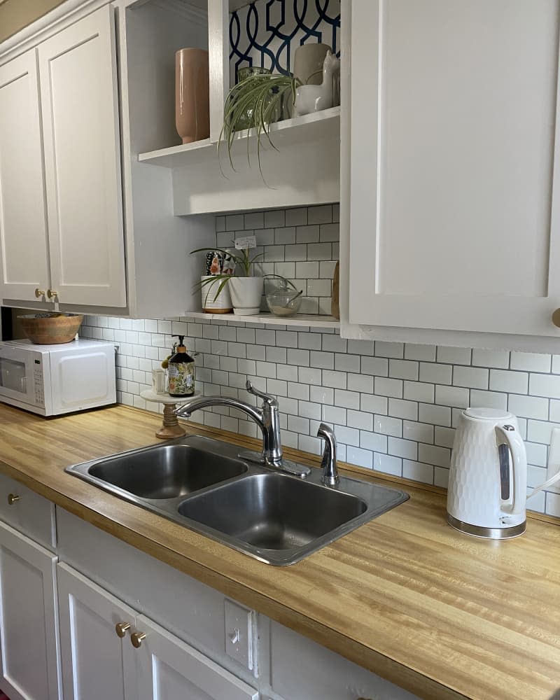 kitchen with pale gray cabinets, white subway tile backsplash, and black and white patterned wallpaper after makeover