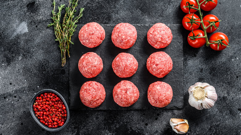 Raw meatballs on a countertop with herbs and vegetables