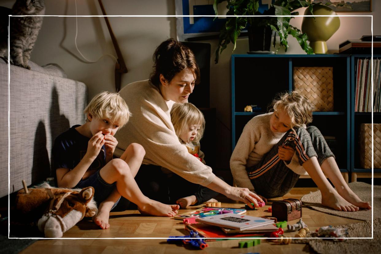  Mother sitting on floor at home playing with her three children. 