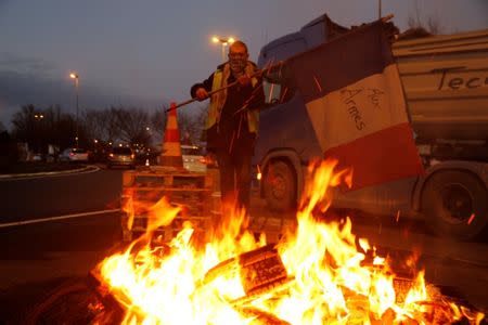 A protester wearing a yellow vest, the symbol of a French drivers' protest against higher diesel fuel prices, holds a flag near burning debris at the approach to the A2 Paris-Brussels Motorway, in Fontaine-Notre-Dame, France, December 4, 2018. REUTERS/Pascal Rossignol