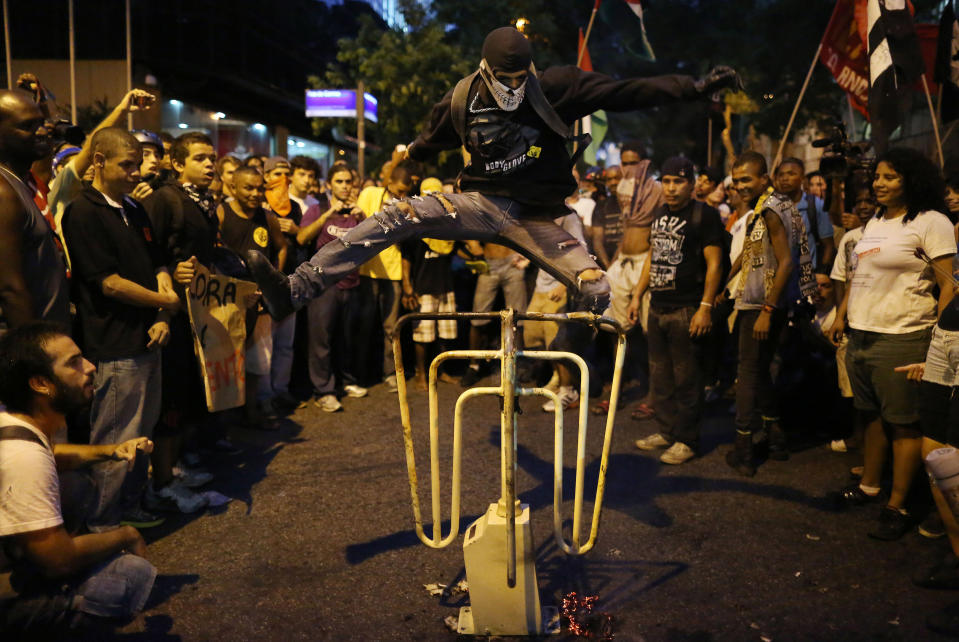 A masked man jumps a bus turnstile set on the street, in protest against the increase on bus fares in Rio de Janeiro, Brazil, Monday, Feb. 10, 2014. Anti-government protests erupted across Brazil last June, hitting their peak as 1 million Brazilians took to streets on a single night, calling for better schools and health care and questioning the billions spent to host this year's World Cup and the 2016 Olympics. The protests have since diminished in size, but remain violent. (AP Photo/Leo Correa)