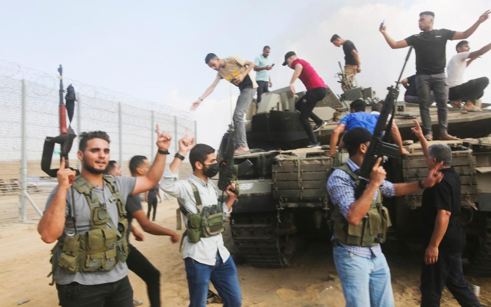 Palestinian militants celebrate by an Israeli tank at the border fence of the Gaza Strip on Saturday, Oct. 7, 2023