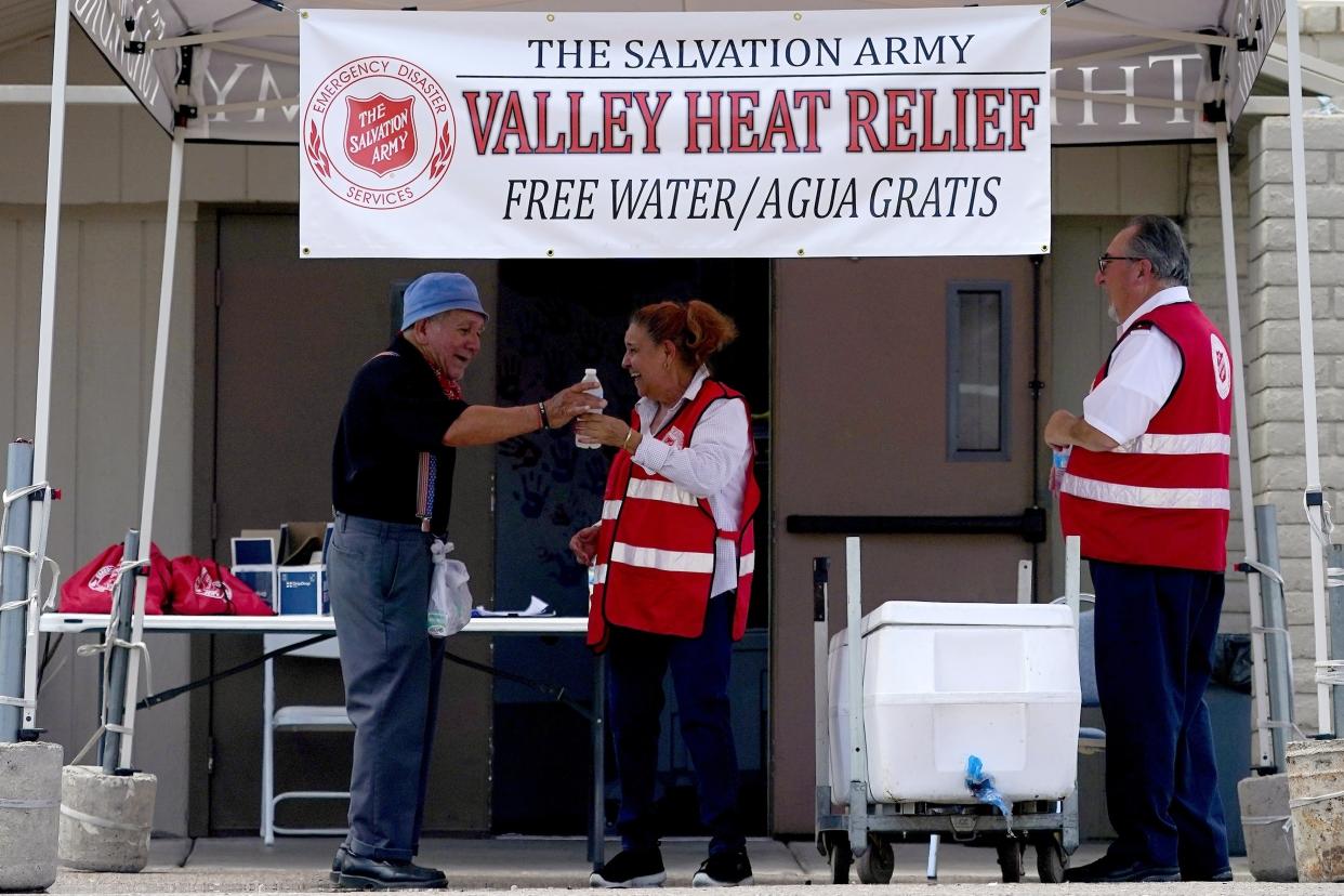 Salvation Army volunteer Francisca Corral, center, gives water to a man at a the organization's heat relief station in Phoenix