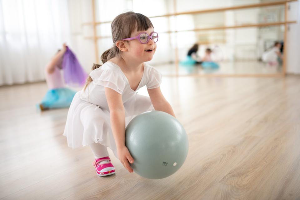 Little girl in a white dress playing with a ball in a ballet studio