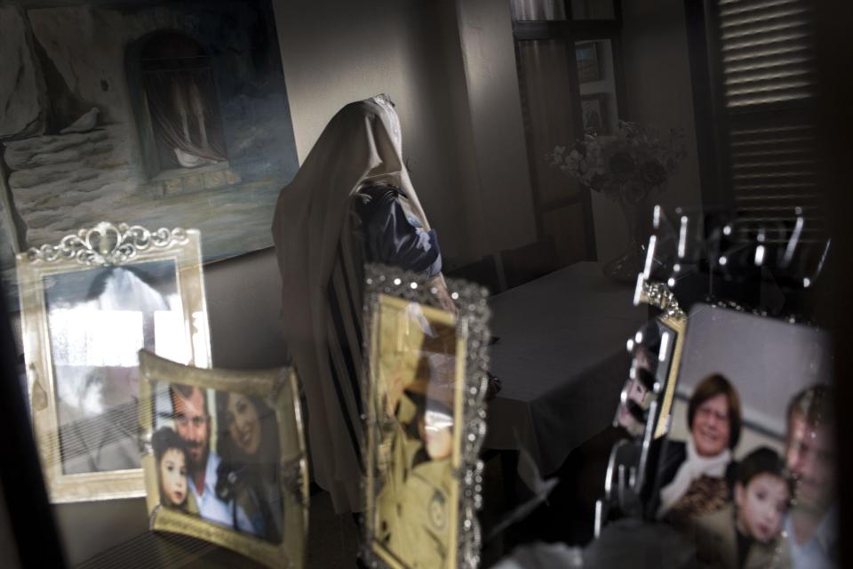 In this photo taken Wednesday, April 30, 2014, Jewish ultra-Orthodox military captain Moshe Prigan, is reflected in a mirror in his library as he prepares for his morning prayer at home in the ultra-Orthodox Jewish town of Bnei Brak, near Tel Aviv, Israel. Prigan doesn't just serve in the military, he also recruits other ultra-Orthodox Jewish men to enlist, something the cloistered community has traditionally avoided doing. The issue of military service is at the core of a cultural war over the place of ultra-Orthodox Jews in Israeli society today. (AP Photo/Oded Balilty)