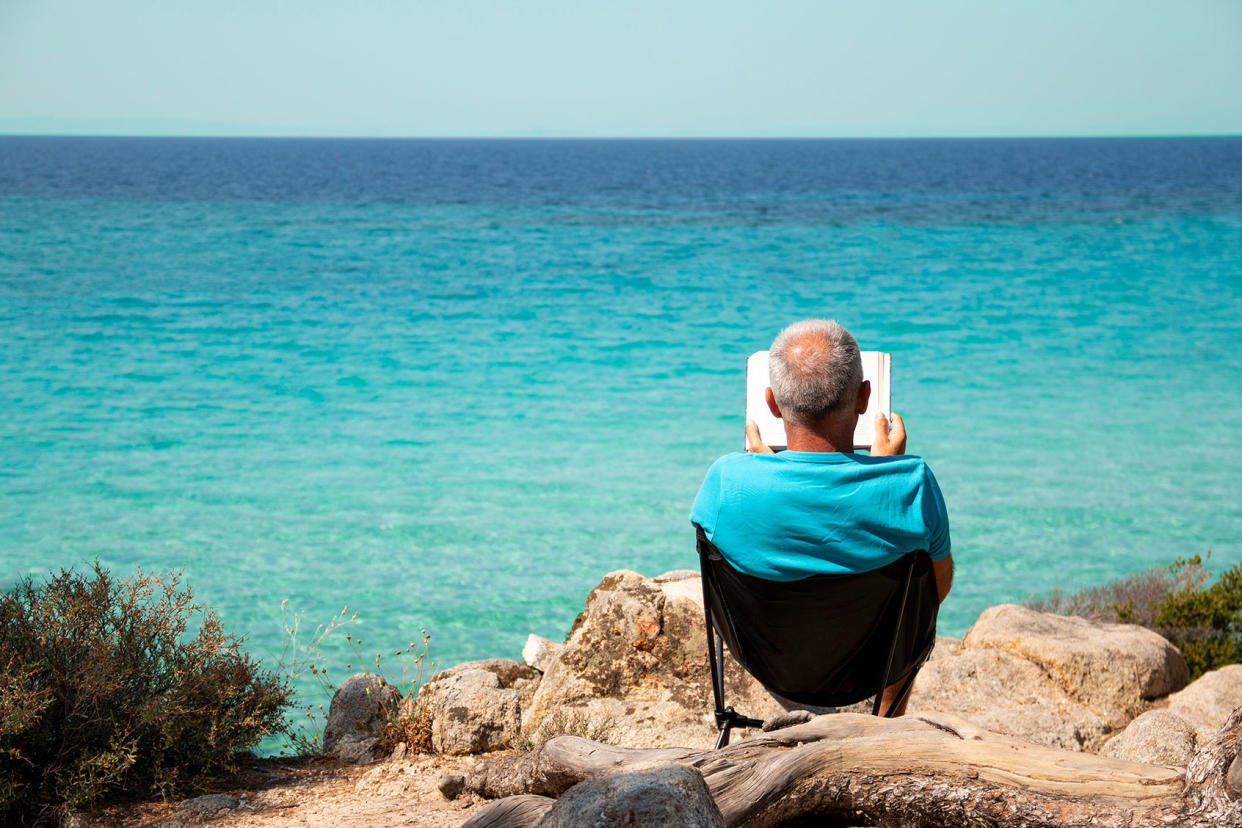 Happy senior man reading next to the Aegean sea Getty Images/Anastasija Vujic