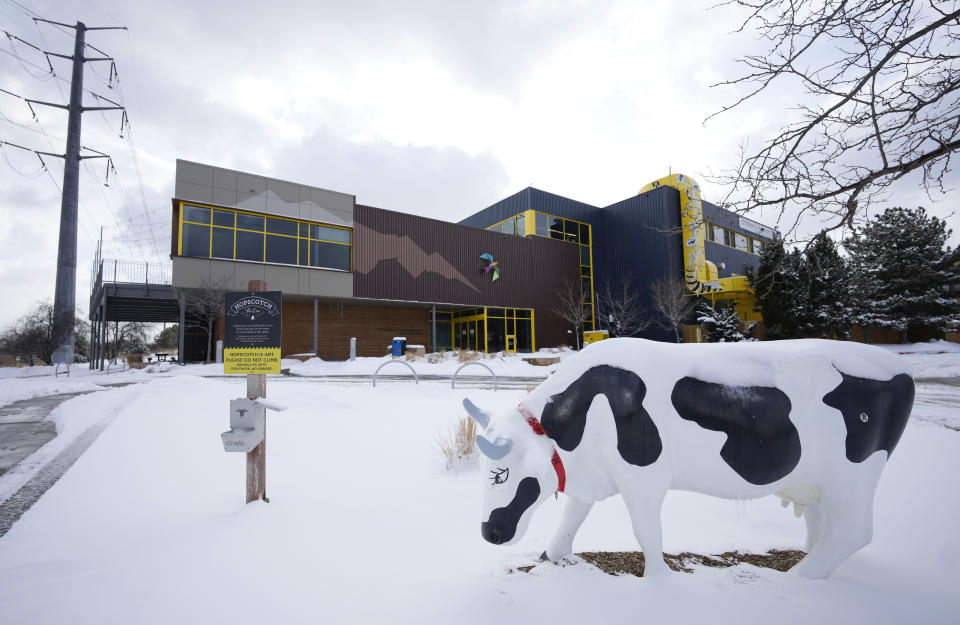 Hopscotch, a chalkboard cow, stands alone in a light snow outside the Children's Museum of Denver at Marsico Campus Thursday, Jan. 27, 2022, in Denver. The popular museum temporarily closed on Wednesday because of escalating harassment of staff by adult visitors angry over a city-ordered mandate requiring anyone age 2 and older to wear a mask in indoor public spaces. The museum will remain closed until Friday, Feb. 4. (AP Photo/David Zalubowski)