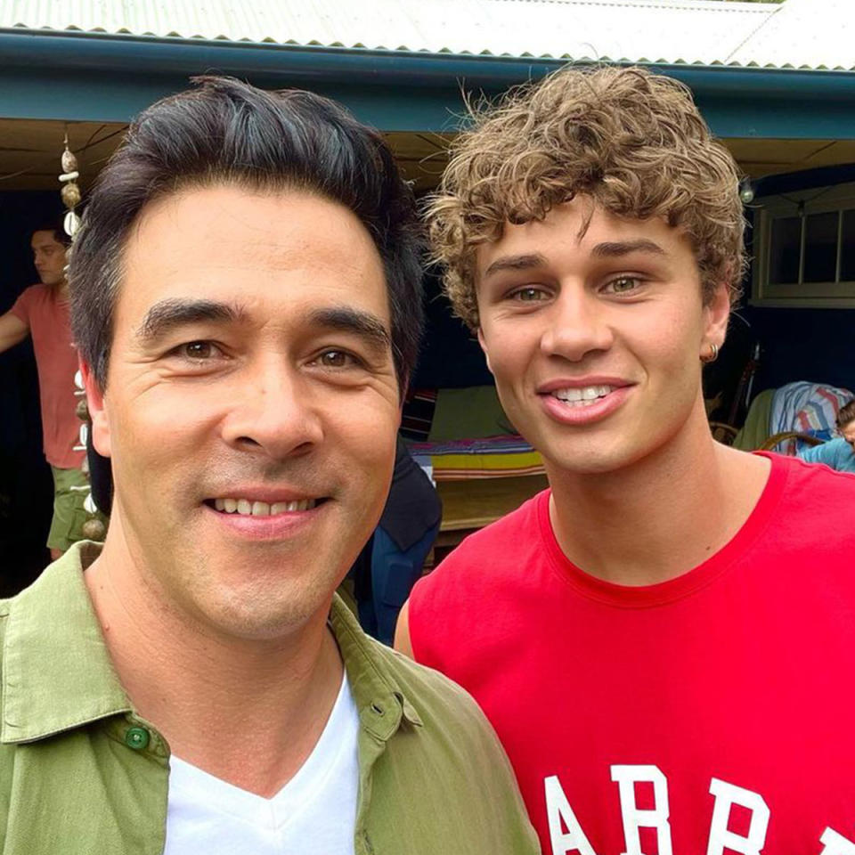 Matt Evans in a red t shirt and James Stewart in a green shirt smile at the camera while filming Home and Away