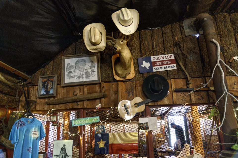 Cowboy hats hang on a deer head next to a portrait of John Wayne at Big John’s Feed Lot in Big Spring, Texas, Friday, Oct. 15, 2021. At the burger and barbecue restaurant the parking lot was filled at lunchtime with gas-guzzling American-made pickup trucks. “Can you imagine anyone in here driving an electric car?” asked Brenda Stansel, the owner, who insisted Trump was still the rightful commander-in-chief. Asked if she believed in climate change, Stansel responded: “I believe in God.” (AP Photo/David Goldman)