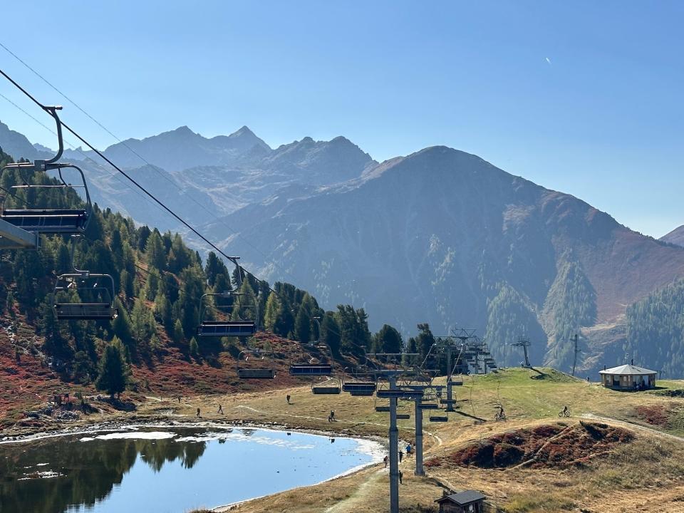 ski lifts hang empty all the way down a slope over a pond with large shaded mountains in the distance