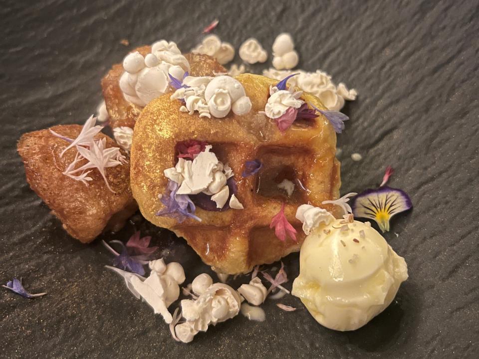 waffle dessert with ice cream and edible flowers on a black plate