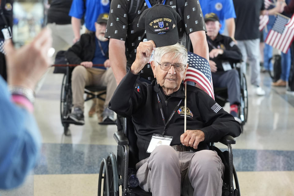 World War II veteran Bob Shipe lifts his hat as he moves along with other veterans before boarding a plane at Dallas Fort Worth International Airport in Dallas Friday, May 31, 2024. A group of World War II veterans are being flown from Texas to France where they will take part in ceremonies marking the 80th anniversary of D-Day. (AP Photo/LM Otero)