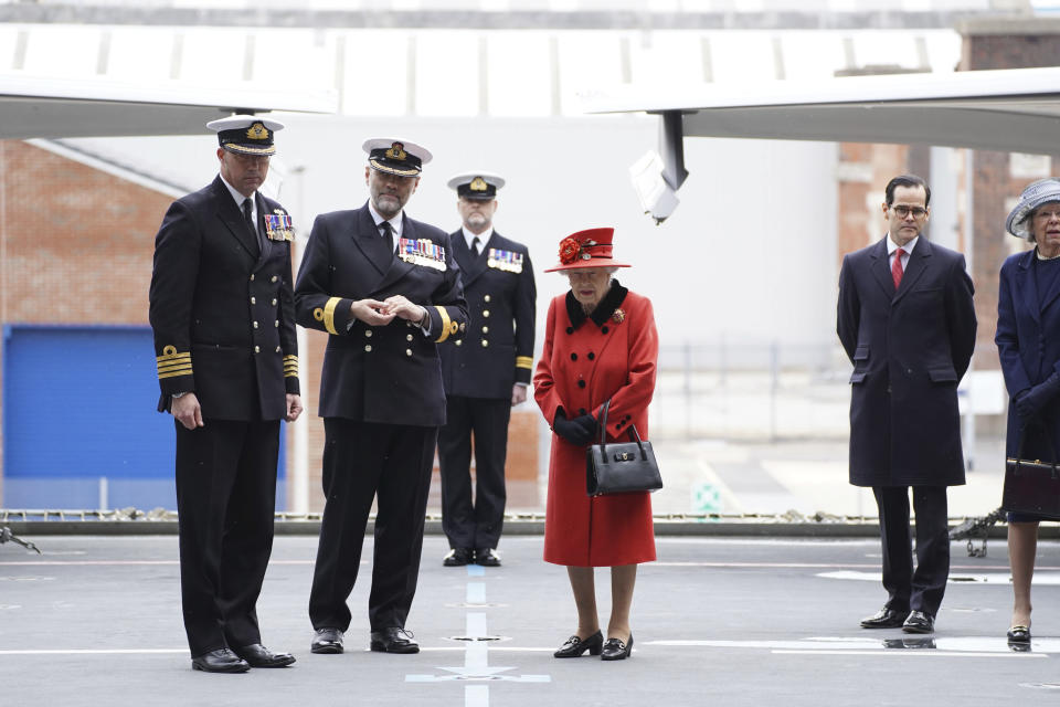 Captain Angus Essenhigh , left, , Commodore Steve Moorhouse, second from left, accompany Britain's Queen Elizabeth II , centre, on the flight deck, during a visit to HMS Queen Elizabeth at HM Naval Base, ahead of the ship's maiden deployment, in Portsmouth, England, Saturday May 22, 2021. HMS Queen Elizabeth will be leading a 28-week deployment to the Far East that Prime Minister Boris Johnson has insisted is not confrontational towards China. (Steve Parsons/Pool Photo via AP)