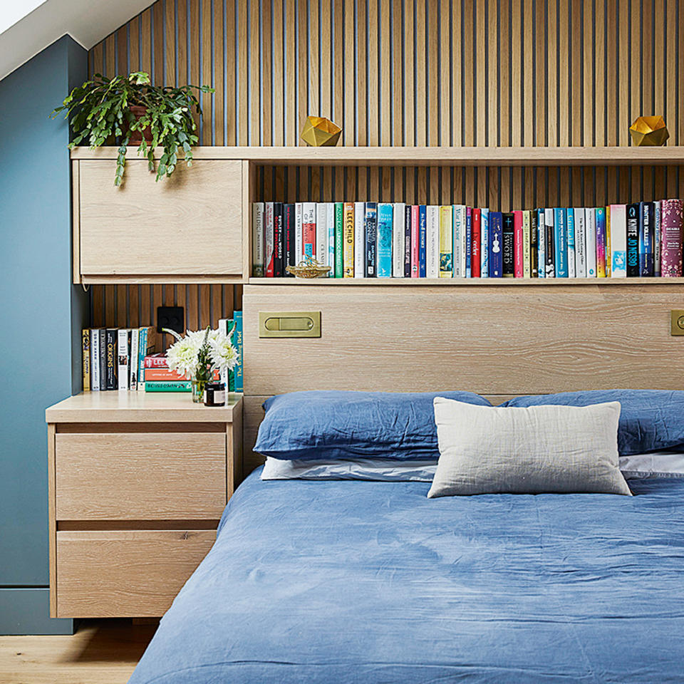 Bedroom with blue walls and wooden shelving and wall panelling above a bed dressed in blue linen bedding