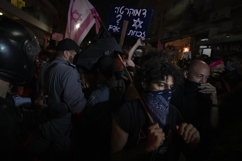 Israeli police officers try to block Israeli protesters during a demonstration against lockdown measures that they believe are aimed at curbing protests against prime minister Benjamin Netanyahu in Tel Aviv, Israel, Thursday, Oct. 1, 2020. The sign in Hebrew reads: "Democracy, human rights" (AP Photo/Sebastian Scheiner)