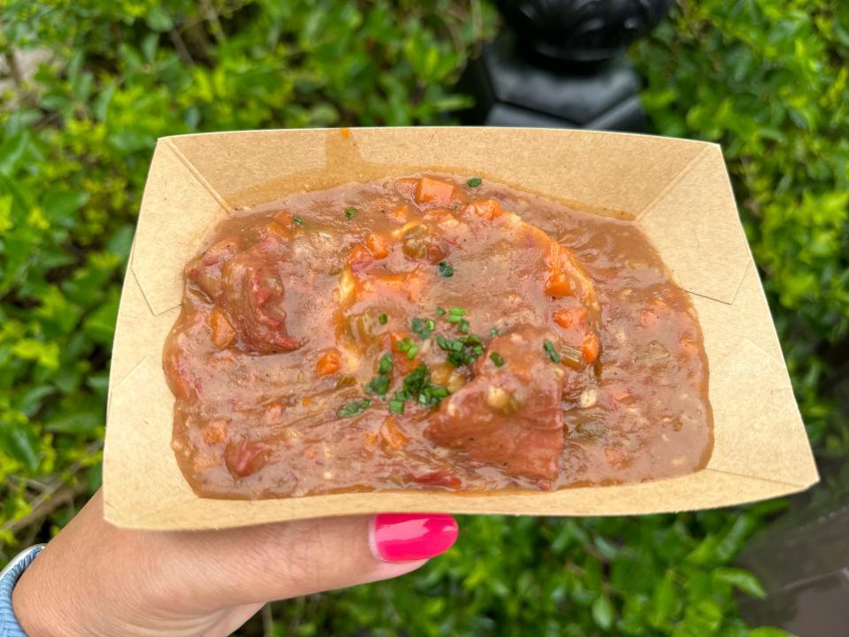 hand holding a bowl of beer braised beef from epcot food and wine