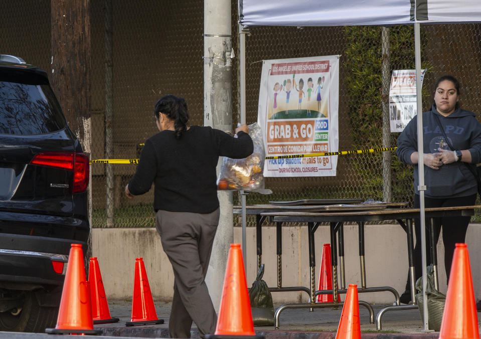 FILE - People step out of their vehicles at a "Grab & Go" stop to get free school meals provided by the Los Angeles Unified District at the Virgil Middle School station in Los Angeles Wednesday, March 25, 2020. Amid spiking coronavirus cases, Los Angeles Unified School District campuses will remain closed when classes resume next month, Superintendent Austin Beutner said Monday, July 13, 2020, defying President Donald Trump's demand that students return to in-person instruction. (AP Photo/Damian Dovarganes, File)