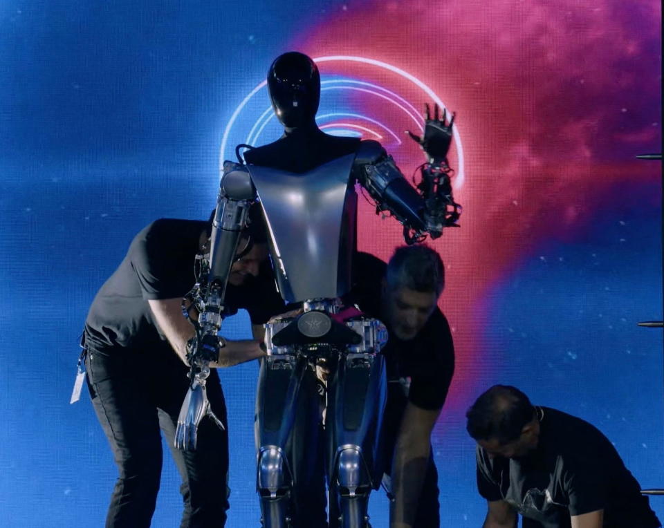Tesla employees set up the newest version of the company's humanoid Optimus robot on stage at Tesla AI Day 2022.