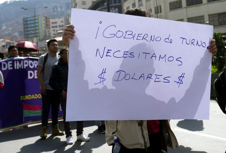 FILE - A merchant holds up a sign with a message that reads in Spanish: "Current government, We need dollars!" during a protest in La Paz, Bolivia, May 17, 2024. With prices surging, dollars scarce and lines snaking away from fuel-strapped gas stations, protests in Bolivia have intensified over the economy's precipitous decline. (AP Photo/Juan Karita, File)