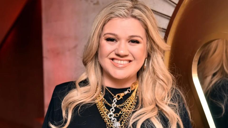 Singer Kelly Clarkson, a woman with light-toned skin and blonde hair, wears a black top and multiple necklaces, mostly gold.