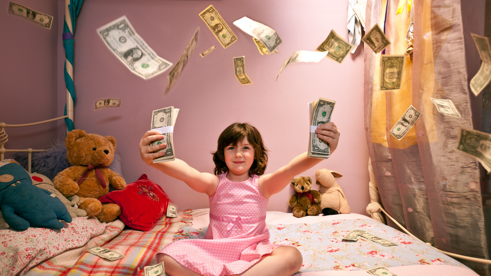 a young girl sitting on her bed in a pink dress with stuffed animals and dollar bills flying all over