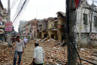 Nepalese people walk past collapsed buildings at Lalitpur, on the outskirts of Kathmandu, on April 25, 2015