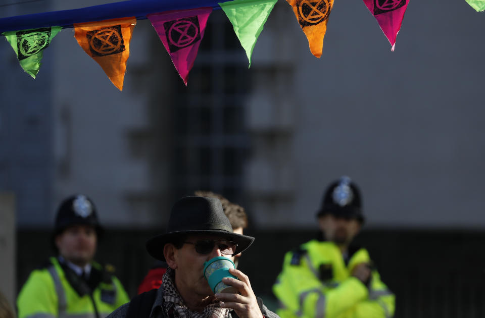 A Climate change protester has a drink watches by two policemen in Whitehall on the second day of ongoing protests in London, Tuesday, Oct. 8, 2019. Police are reporting they have arrested more than 300 people at the start of two weeks of protests as the Extinction Rebellion group attempts to draw attention to global warming.(AP Photo/Alastair Grant)