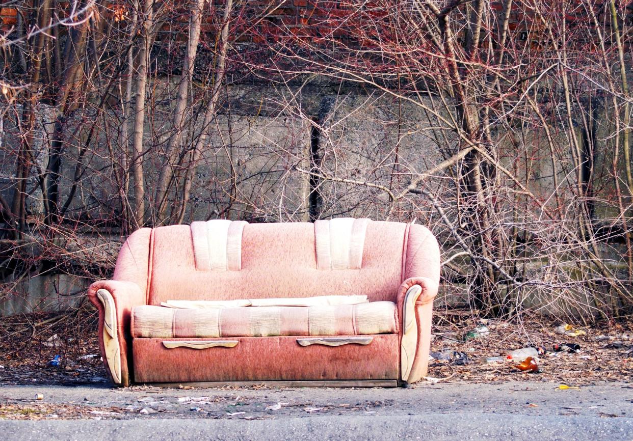 Lonely dirty abandoned sofa, left in the street with junk