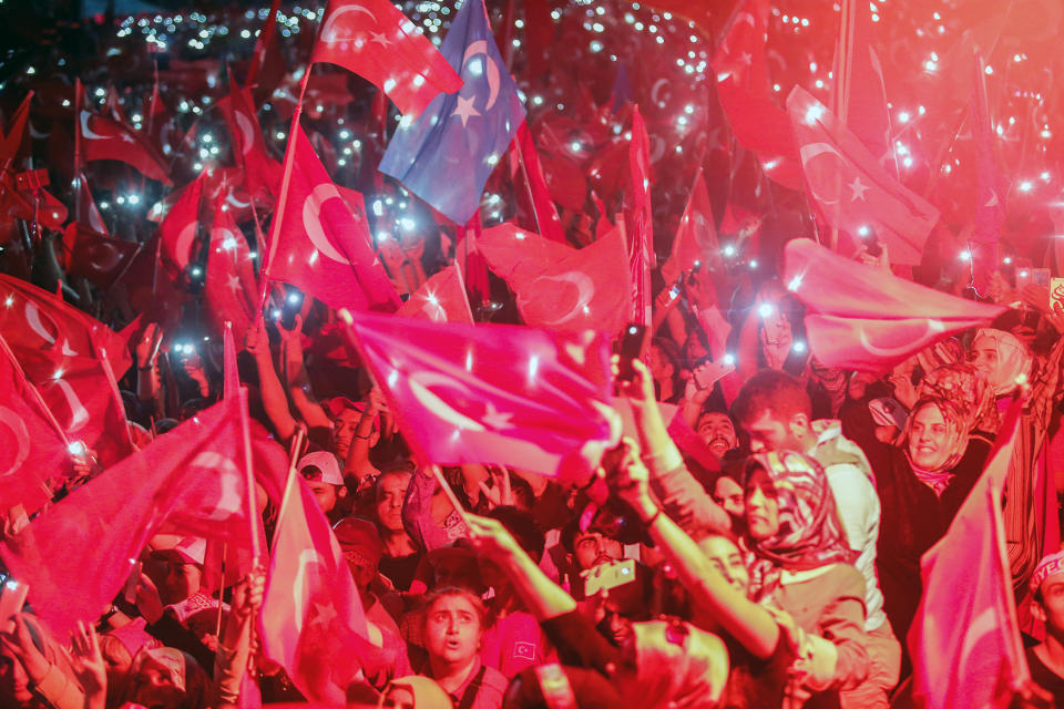 Turkish people wave flags of their country and use the lights of their cell phones