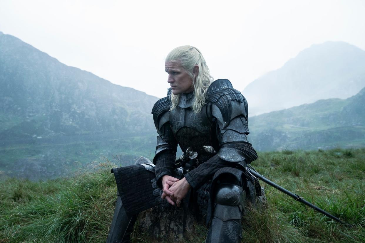 matt smith as daemon targaryen in house of the dragon. he has black armor on, and blonde hair pulled half back. he looks worried and is sitting on a hill