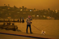 A man walks his dog along Bridgeway Avenue as smoke from wildfires darken the morning Wednesday, Sept. 9, 2020, in Sausalito, Calif. (AP Photo/Eric Risberg)