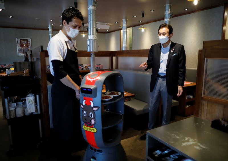 Miki Watanabe, Chairman and CEO of Watami Co. talks with a staff member next to a serving robot at their yakiniku barbecue restaurant named 'Yakiniku no Watami', in Tokyo