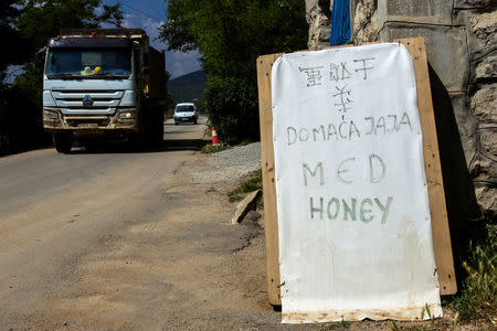 Construction trucks pass by a board advertising homemade eggs and honey in Chinese, Montenegrin and English on the Bar-Boljare highway construction site in the village of Pelev Brijeg, Montenegro June 11, 2018. REUTERS/Stevo Vasiljevic