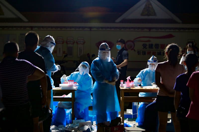 Medical workers attend to people lining up for nucleic acid testing at a residential compound in Ruili